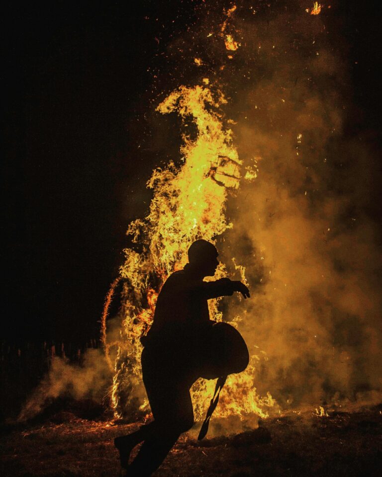 Dramatic silhouette of a man running against the backdrop of a large blazing fire at night.