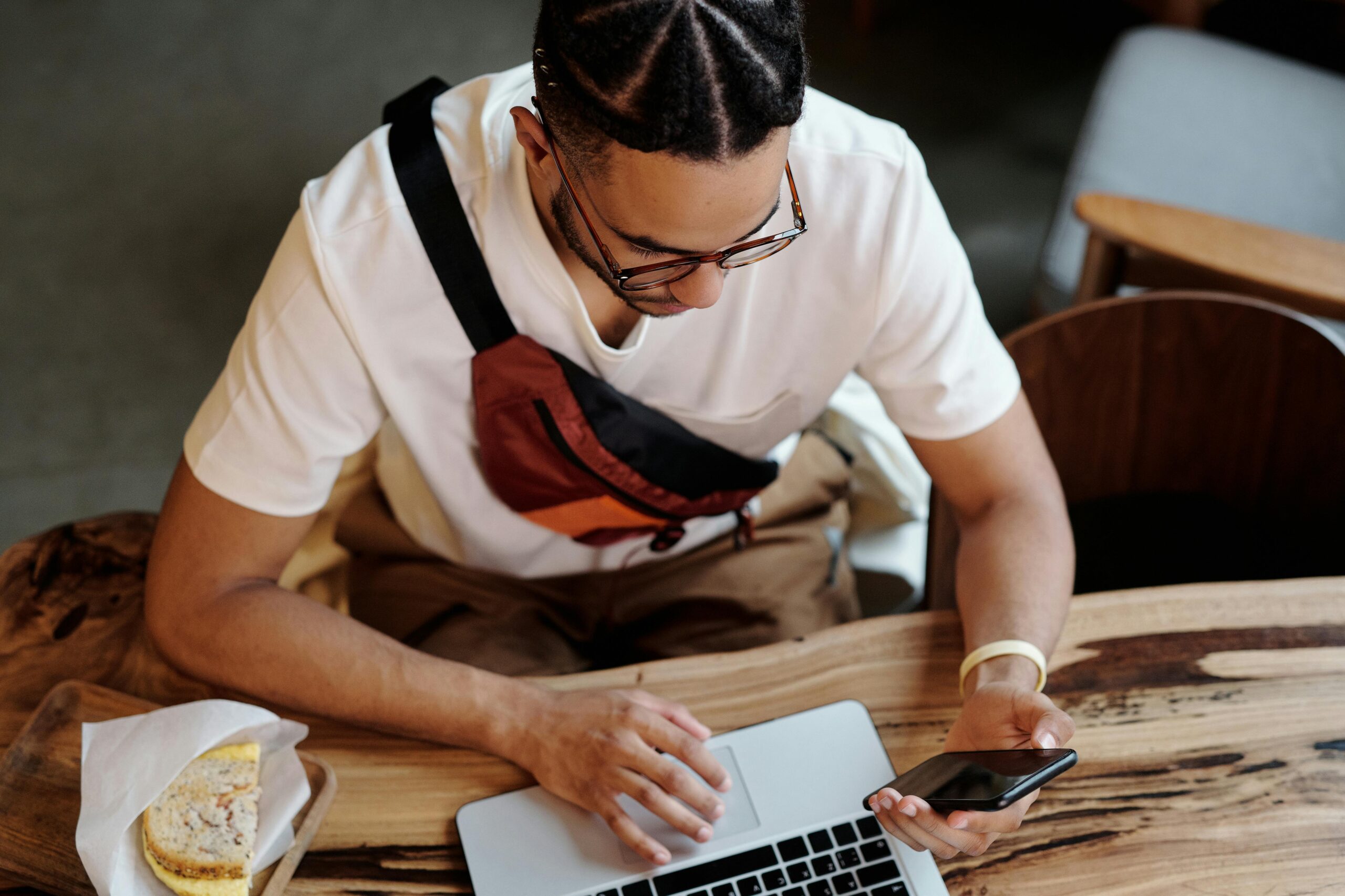 A focused freelancer uses a laptop and smartphone while sitting at a cafe table indoors.